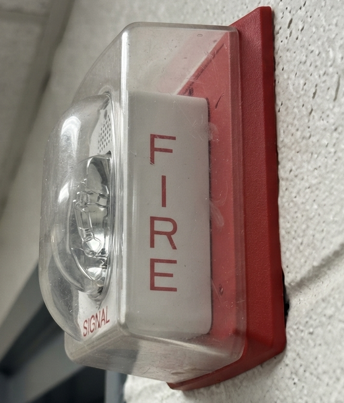 A red fire alarm strobe light mounted on a wall, labeled FIRE